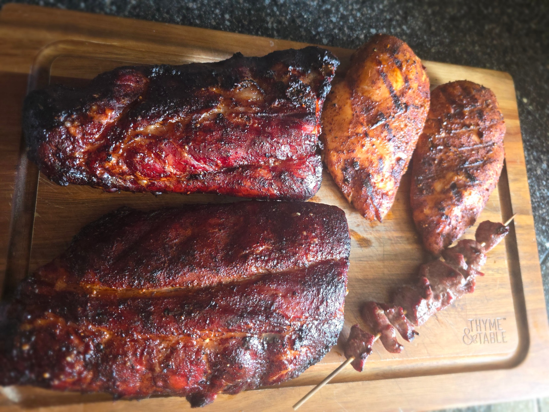 Smoked brisket, grilled chicken, and beef skewers on a wood board